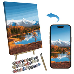 Canvas diamond painting kit showing a completed mountain lake landscape on an easel, a smartphone displaying the matching design, paint bottles, and paintbrushes on a white background with a blue arrow indicating the design-to-canvas process.