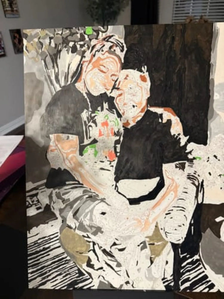 An expressive, textured painting of two people embracing, displayed on a stand in an indoor setting. The artwork features bold black, white, gray, and peach tones with splashes of green and orange.